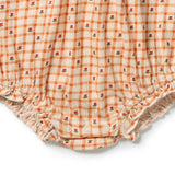 Close-up of a baby romper or diaper cover made of textured gauze fabric, featuring an orange and cream gingham check pattern with small red rose motifs and ruffled elastic leg openings.