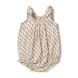 A sleeveless baby romper in cream-colored fabric with a small, dense multicolor floral and leaf print, featuring a smocked bodice and ruffled neckline and leg openings.