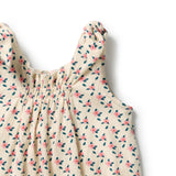 Close-up of a sleeveless baby dress with a smocked bodice and ruffled shoulder straps, featuring a pink and green floral print on a cream-colored textured fabric, set against a plain white background.