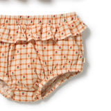 A close-up of a baby bloomers diaper cover featuring an orange and cream gingham pattern with small red rose prints, complete with a ruffled waistband, on a white background.