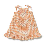 A sleeveless toddler girl's dress featuring an orange and beige gingham pattern with tiny floral details, tie shoulder straps, and a ruffled hem, shown on a white background.