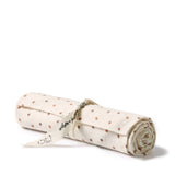 A rolled cream-colored muslin cloth or swaddle with small brown polka dots, tied with a cream ribbon printed with black text and cat illustrations, on a white background.
