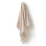 A cream-colored baby blanket with a small brown polka dot pattern, hanging against a plain white wall.