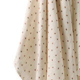 A close-up of a cream-colored muslin fabric with a small brown leaf pattern, draped against a plain white background.