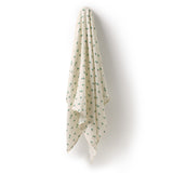 An off-white muslin baby blanket with a small green floral pattern, hanging against a plain white wall.