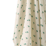 A close-up of a cream-colored crinkled fabric, likely a muslin baby blanket or swaddle, printed with a small green palm tree pattern.