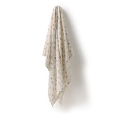A cream-colored baby blanket with a delicate gray and black floral pattern, hanging from a hook on a plain white wall.