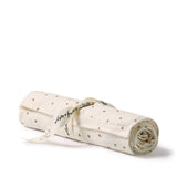 An off-white muslin baby blanket rolled up and tied with a white ribbon printed with black text, featuring small brown embroidered motifs, on a white background.