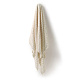 A cream-colored muslin baby blanket with small black polka dots, hanging from a wall hook against a white background.