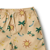 Close-up of a pair of beige swim shorts with a tropical print featuring palm trees, smiling suns, bananas, and blue fish, complete with a white drawstring waist.