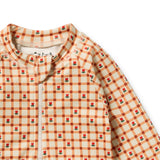 Close-up of a long-sleeve baby garment with a cream and orange gingham check pattern, decorated with small red rose motifs, featuring a white zipper at the neckline.