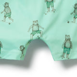 Close-up of mint green swim trunks with an all-over print of teddy bears wearing green-and-white striped swim trunks and skateboarding, shown against a white background.