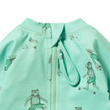 A close-up of a mint green zippered jacket featuring a playful print of teddy bears wearing green-and-white striped shorts and riding skateboards.