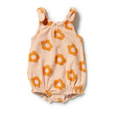 A baby romper in a soft peach-beige color with a repeating orange flower pattern, featuring a gathered elastic neckline and ruffled shoulder straps, laid flat on a white background.