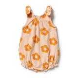 A baby romper in a soft peach fabric with an orange flower pattern, featuring ruffled shoulder straps and a ruffled hem, laid flat on a white background.