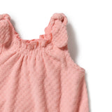 Close-up of a baby girl's sleeveless romper in a dusty pink color, featuring a textured waffle-weave pattern, a ruffled smocked neckline, and decorative ruffle details on the shoulder straps, shown on a plain white background.