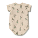 A short-sleeve baby bodysuit in a warm beige fabric, featuring an all-over print of teddy bears playing soccer in muted green and gray tones, laid flat on a white background.