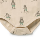 Close-up of a beige baby bodysuit featuring an all-over print of teddy bears wearing green striped shorts and riding skateboards, finished with snap closures at the crotch.
