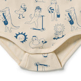 Close-up of a baby bodysuit or diaper cover in warm cream with a navy blue cartoon print, showing playful illustrations of animals, a sun, and objects on a white background.