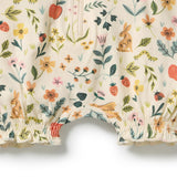 Close-up of a children's romper or shorts with an all-over spring floral print on a cream base. The pattern features green leaves, orange and yellow flowers, strawberries, ladybugs, a rabbit, a bird, and a caterpillar.