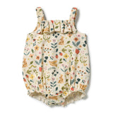 A baby romper with a cream-colored background and a colorful print of bunnies, flowers, and birds, featuring ruffled straps and a ruffled hem.