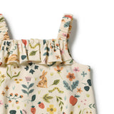 Close-up of a children's sleeveless top with ruffled straps and a cream base fabric printed with a whimsical woodland pattern of a rabbit, flowers, leaves, caterpillars, and strawberries.