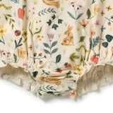Close-up of a cream-colored baby romper with a whimsical floral and animal print, featuring a rabbit, bird, flowers, leaves, and caterpillars, finished with a ruffled hem.