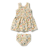 A baby girl's two-piece outfit set consisting of a sleeveless smocked dress and matching bloomers, featuring a colorful woodland animal and floral print on a cream-colored background.