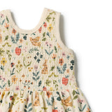 Close-up of a sleeveless smocked dress with a cream base and a colorful floral and nature print featuring butterflies, birds, and wildflowers.