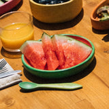 Sliced watermelon in a green bowl on a wooden table with a glass of orange juice.