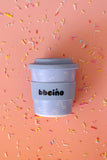 Blue coffee cup with 'bbecca' branding on a pink background with sprinkles