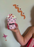 Pink cup with cherry design held by a child against a white wall with decorative elements.
