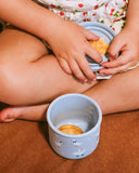 Child's hands interacting with a small blue container on a brown surface
