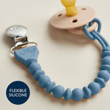 Blue silicone teether with a pacifier clip on a beige background