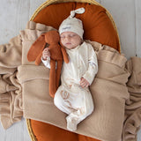 Newborn baby in a Moses basket with a brown plush toy, wearing a white hat and onesie.