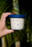 Hand holding a container with a blue lid against a blurred natural background