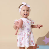 Child wearing a floral dress holding a doll against a beige background