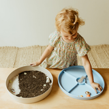 Child playing with a sensory bin and blue tray on a wooden table.