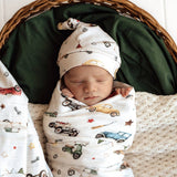Newborn baby swaddled in a blanket with car patterns, wearing a matching hat, in a wicker basket.