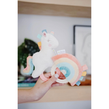 Hand holding a soft toy with a unicorn design and rainbow colors.