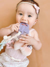 Baby holding a purple teething toy with a plain background