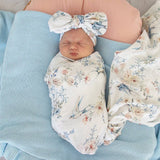 Newborn baby wrapped in floral fabric with matching headband on a blue blanket