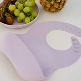 Purple bib on a white surface with grapes and a pineapple in the background