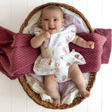 Baby in a floral dress lying on a pink blanket in a wicker basket.
