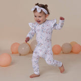 Baby in a floral onesie standing among balloons on a beige background