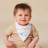 A smiling baby wearing a beige ribbed short-sleeve bodysuit and a white triangular bandana bib with a blue whale and yellow fish print, posed against a solid beige background.
