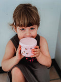 Child holding a pink cup with a pattern against a light blue wall.