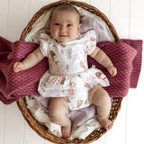 Baby in a floral dress sitting in a wicker basket with pink blankets