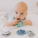 Baby lying on a white blanket with blue silicone teething rings.