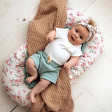 Baby lying on a floral cushion with a brown blanket